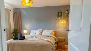 Een slaapkamer met een bed, nachtkastje, lamp en hangplanten.
