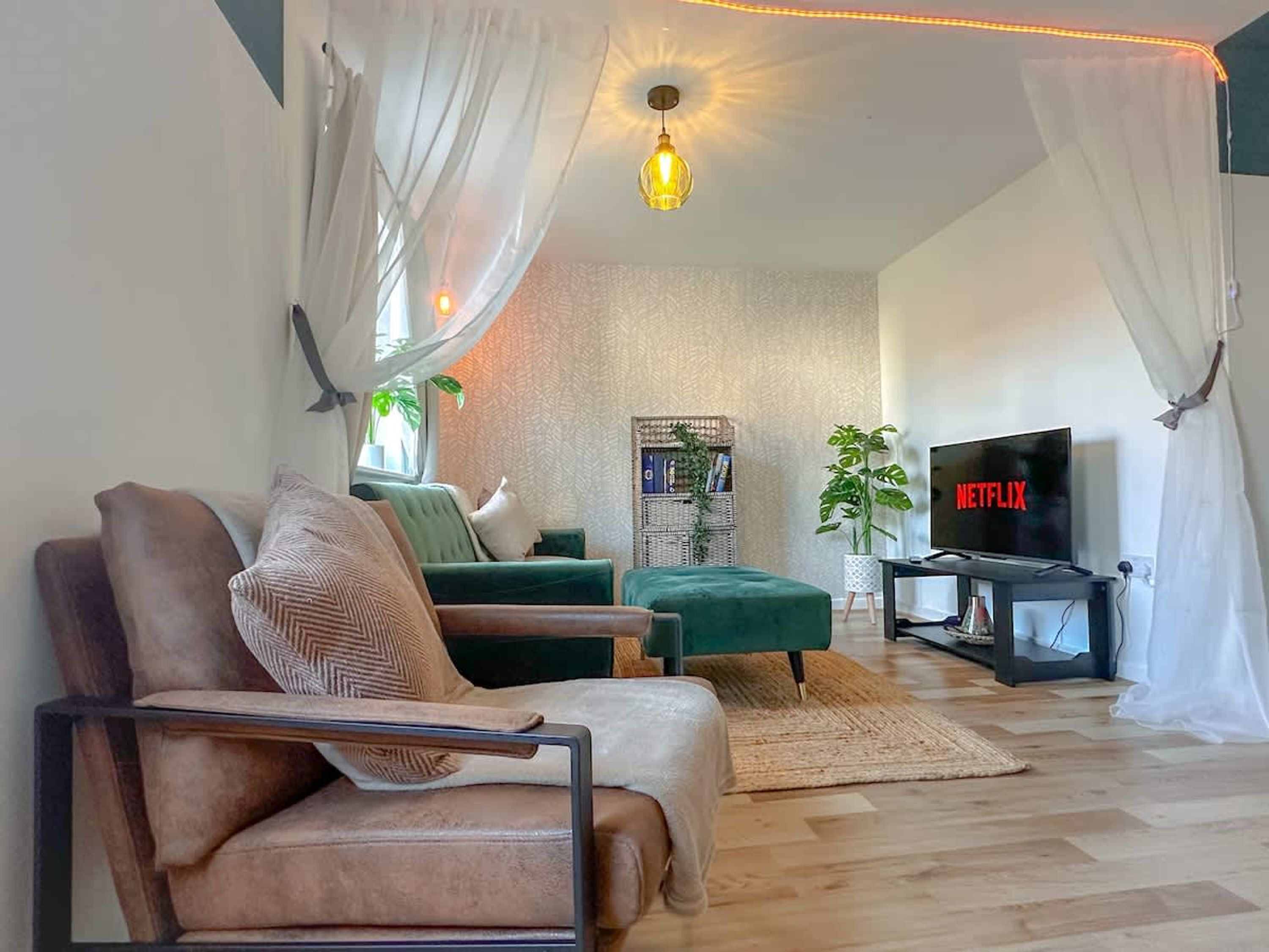 A living room with a sofa, a green ottoman, a TV on a stand, and a hanging light fixture.
