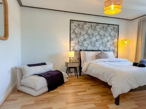 A bedroom with a bed, a nightstand, a lamp, a sofa, and a wall with a floral pattern. - Perfect Booking 3 Bed Home in Central Bracknell (Wokingham)