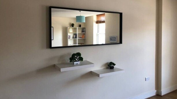 A room with a large mirror, a white shelf with two potted plants, and a white wall. - Spacious 2-bed Flat by Stockwell Station (London)
