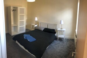 Quarto com cama, duas mesas de cabeceira, guarda-roupa e uma luminária em cada mesa.