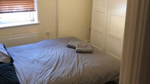 A small bedroom with a single bed, a window with blinds, a white wardrobe, and a hanging light fixture. - Spacious 2-bed Flat by Stockwell Station (London)