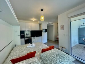 A modern bedroom with a patterned bedspread, a television in the adjacent living area, and a sliding glass door to the outside. - Charming Studio With Parking Near Monaco (Beausoleil)