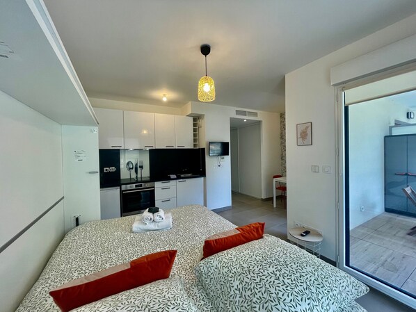A modern bedroom with a patterned bedspread, a television in the adjacent living area, and a sliding glass door to the outside. - Charming Studio With Parking Near Monaco (Beausoleil)