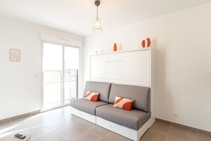 A modern living room with a grey sofa, orange cushions, a white cabinet, and a pendant light. - Charming Studio With Parking Near Monaco (Beausoleil)