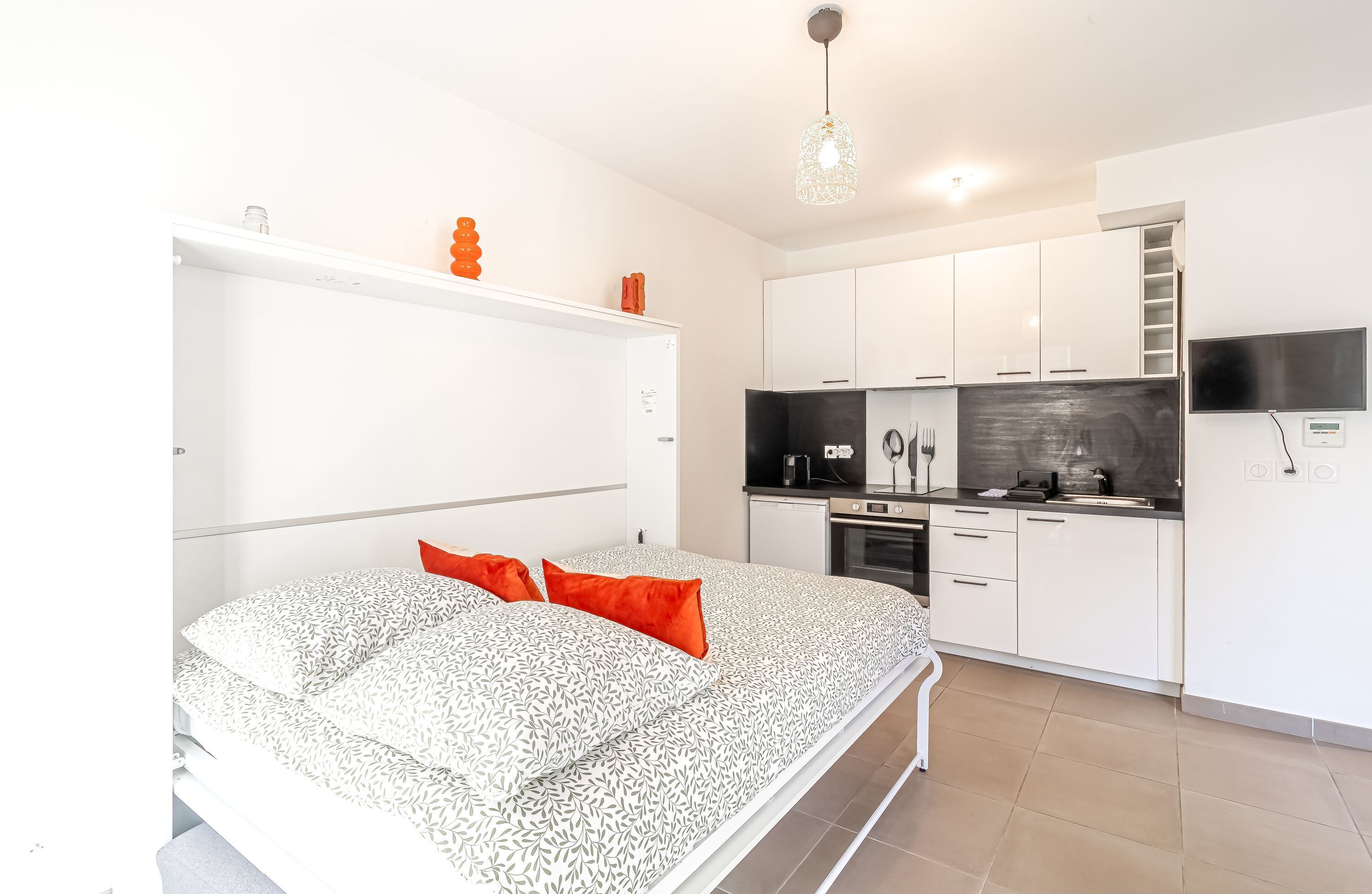 Een slaapkamer met een bed, een witte kast, een keuken met apparatuur en een tv die aan de muur is bevestigd.