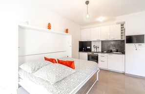 A bedroom with a bed, a white wardrobe, a kitchen with appliances, and a TV mounted on the wall. - Charming Studio With Parking Near Monaco (Beausoleil)