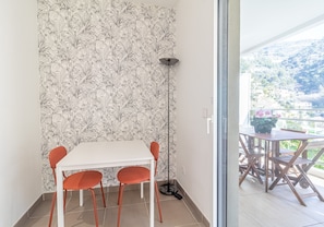 A dining area with a white table and orange chairs, a patterned wallpaper, a floor lamp, and a view of a balcony with outdoor furniture. - Charming Studio With Parking Near Monaco (Beausoleil)