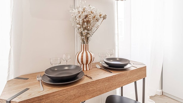 A dining table with two plates, a vase with dried flowers, and a flat-screen TV mounted above. - Nice Studio Close to Monaco (Beausoleil)