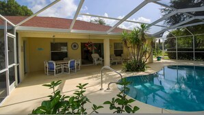 Área de piscina coberta com piscina, cadeiras e um pequeno edifício com telhado vermelho.