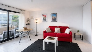 Een moderne woonkamer met een rode bank, een klein wit tafeltje en een glazen eettafel met stoelen.