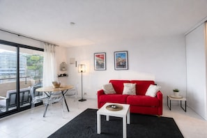 A modern living room with a red sofa, a small white table, and a glass dining table with chairs. - 1BR Sea Monaco View Terrace (Beausoleil)