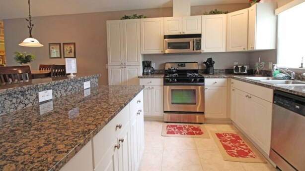 A kitchen with granite countertops, stainless steel appliances, white cabinets, and a red rug. - Wedding Venue View Apartment (Inverness)