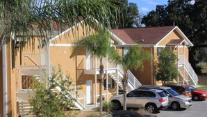 A building with a staircase, a parking lot with cars, and palm trees. - Wedding Venue View Apartment (Inverness)