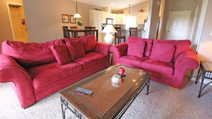 A living room with two red sofas, a glass coffee table, and a dining area in the background. - Wedding Venue View Apartment (Inverness)