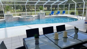 Un espace piscine extérieur abrité, avec une table et des chaises en verre, entouré d’une pergola blanche.