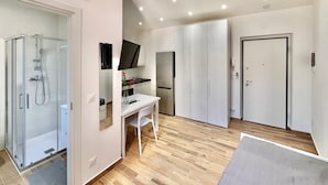 Et moderne hotelværelse med bruser, skrivebord, fladskærms-tv og garderobeskab.
