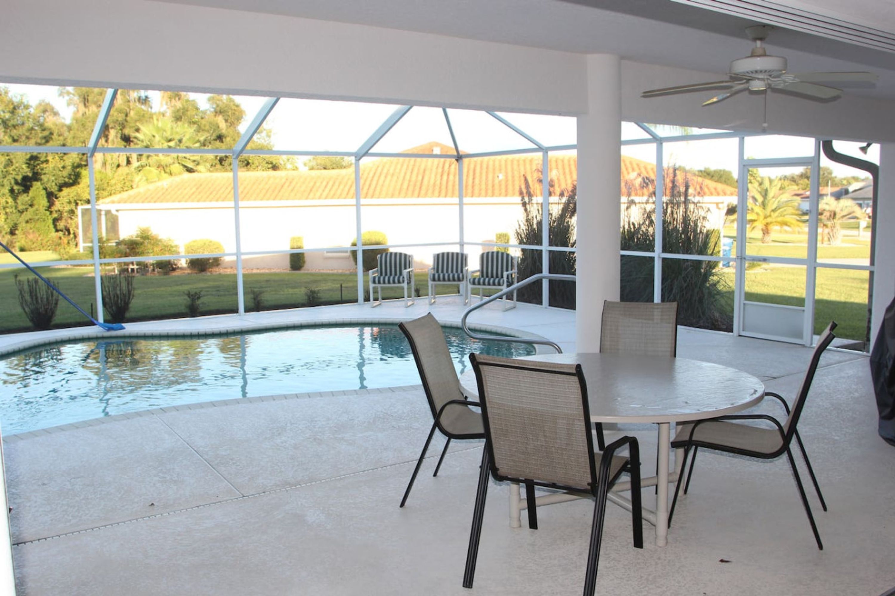 A covered patio with a pool, chairs, and a table.