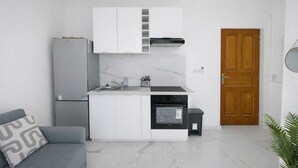 A compact kitchen with white cabinets, a built-in oven, a refrigerator, and a wooden door. - Bright Studio Flat in Cap d Ail - Near Monaco (Cap d'Ail)