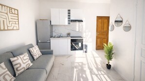 A modern kitchen with white cabinets, a built-in oven, and a grey sofa with patterned cushions. - Bright Studio Flat in Cap d Ail - Near Monaco (Cap d'Ail)