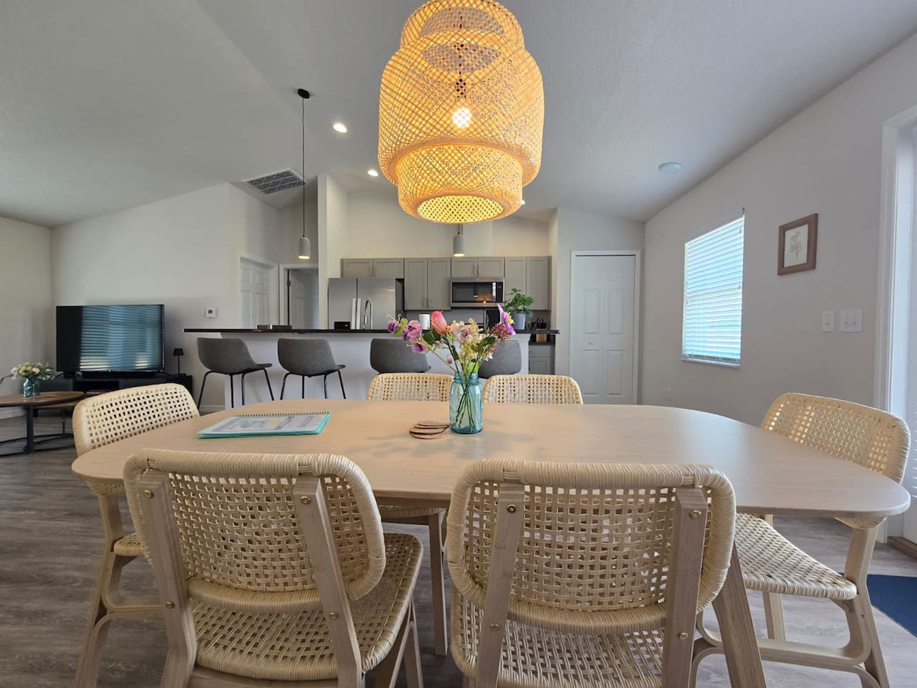 A modern kitchen with grey cabinets, a central island, and a dining area with wicker chairs and a table.