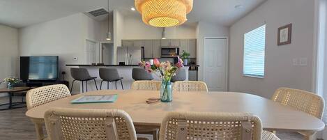 A modern kitchen with grey cabinets, a central island, and a dining area with wicker chairs and a table.