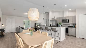A modern kitchen with white cabinets, a central island, and a dining area with a wooden table and wicker chairs.