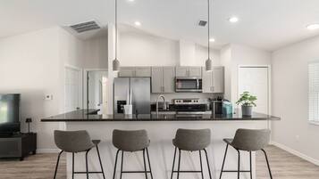A modern kitchen with a central island, bar stools, stainless steel appliances, and pendant lighting.
