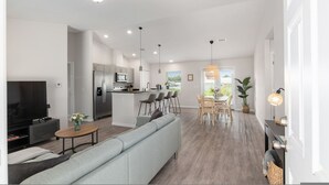 A modern living room with a sofa, TV, and dining area with chairs and a table. - Villa Verde Cozy Home In New Community (Inverness)