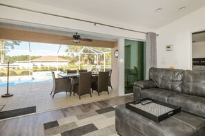 Ein modernes Wohnzimmer mit Ledersofa, einem Essbereich mit Korbmöbeln und Blick auf einen Swimmingpool.