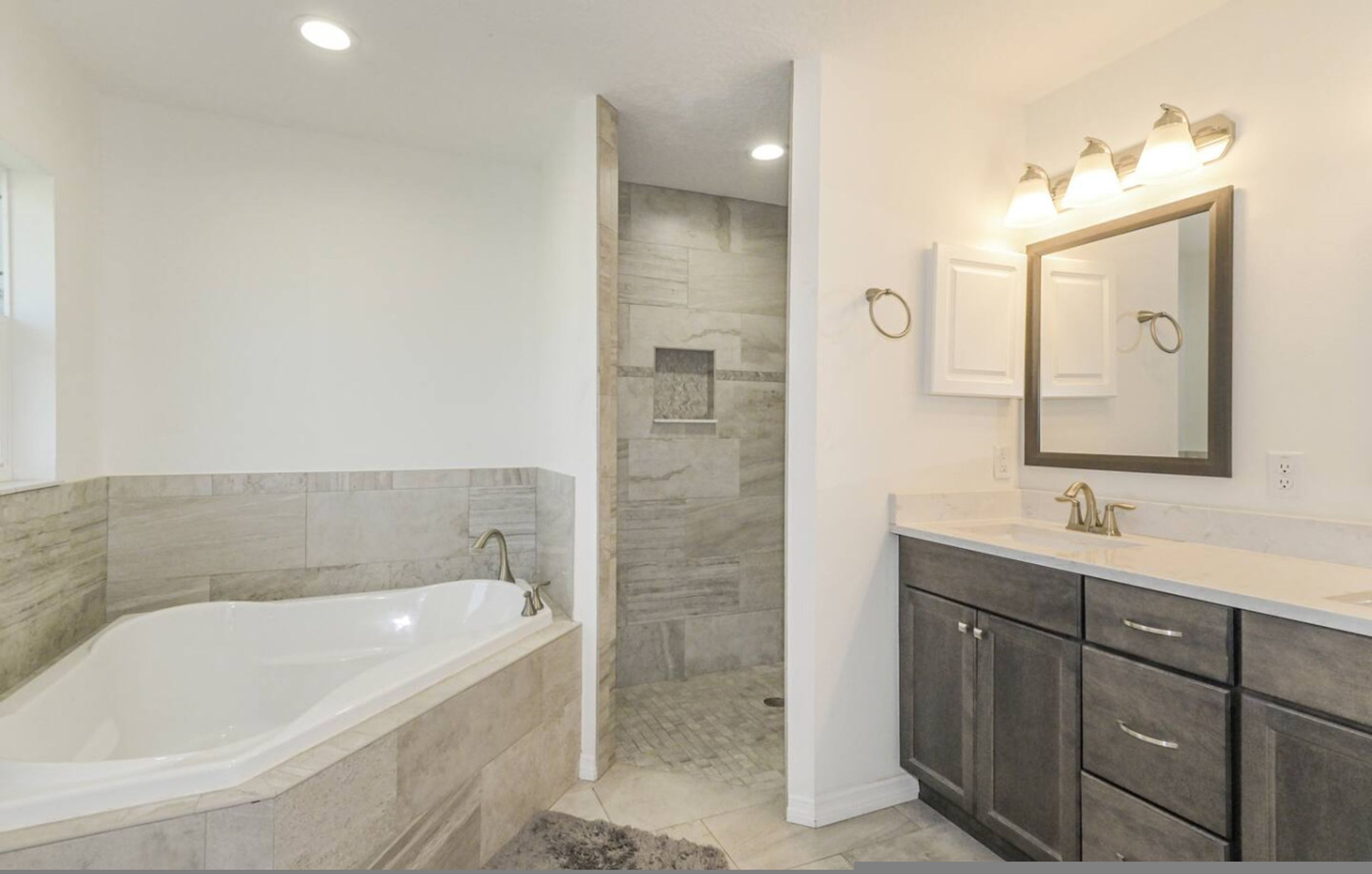 A bathroom with a bathtub, shower, vanity with a mirror, and a towel ring.