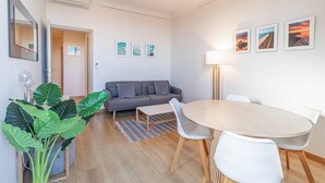 Una sala de estar moderna con un sofá, una mesa de comedor, sillas, una planta en maceta e imágenes enmarcadas en la pared.