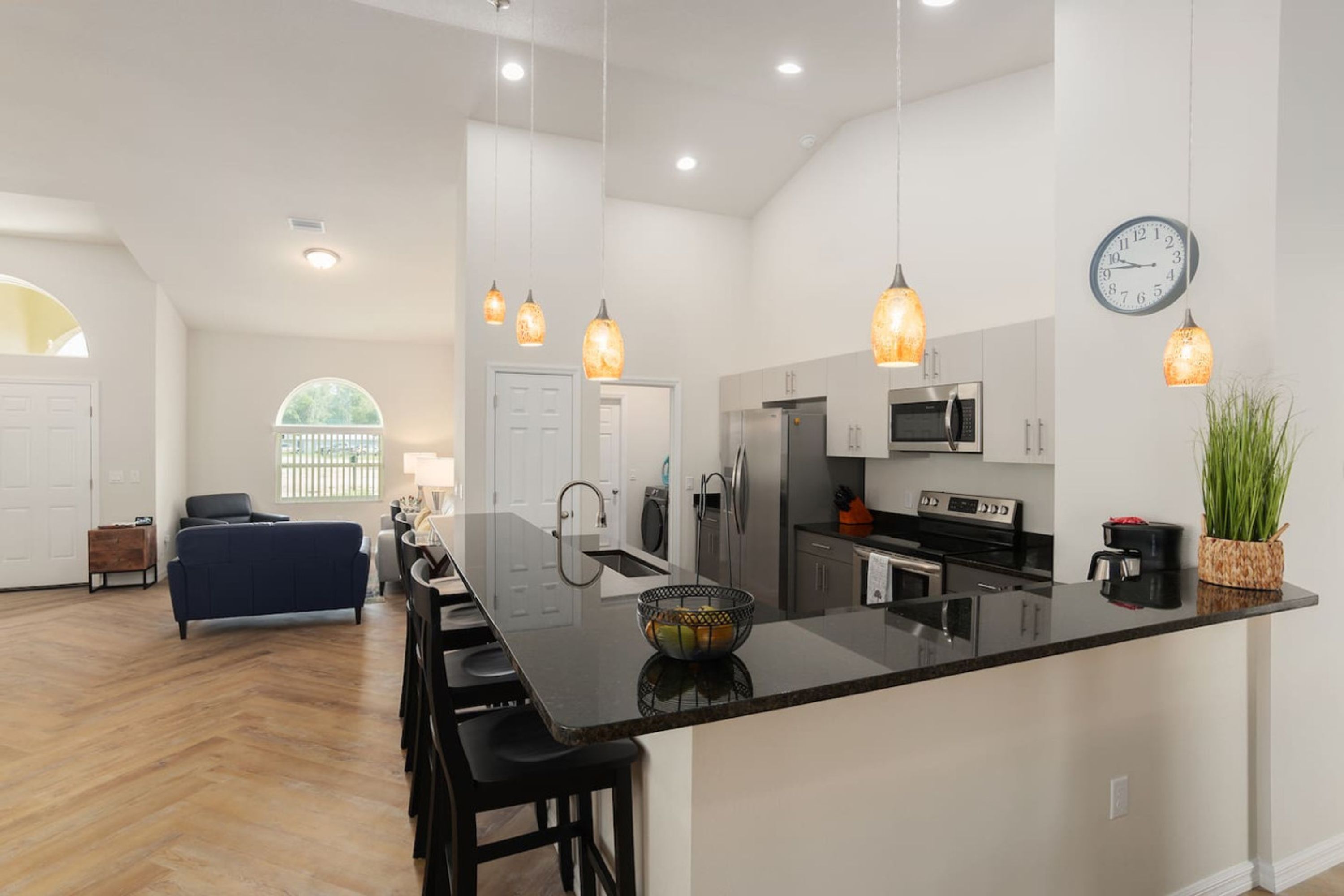 A modern kitchen with a central island, pendant lights, and a clock on the wall.