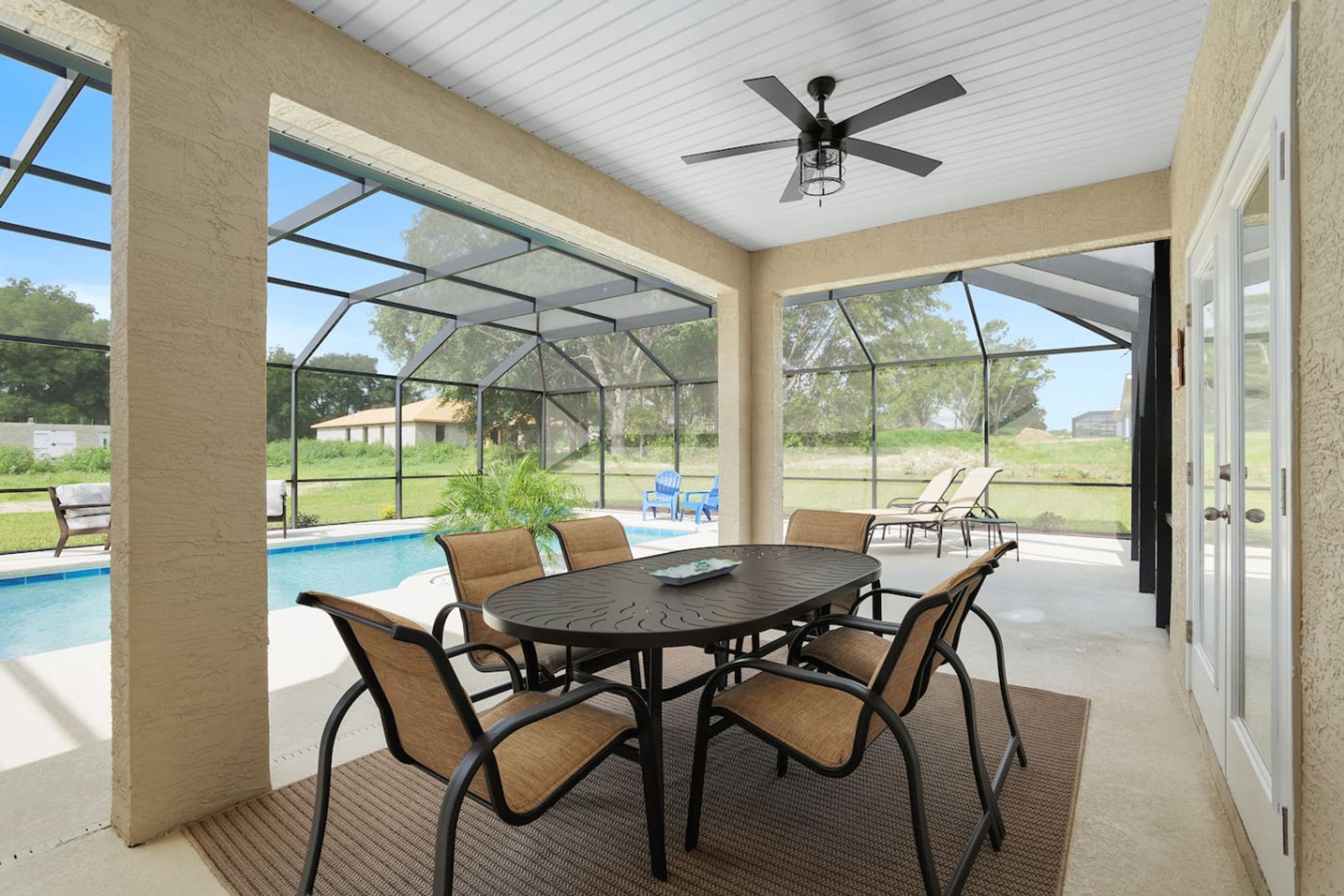 Un patio couvert avec une piscine, des sièges d’extérieur et un ventilateur de plafond.
