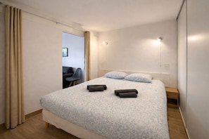 Ein Hotelzimmer mit Bett, Vorhängen, einem Sessel und einem Nachttisch.