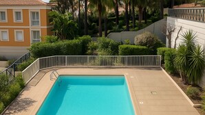Ein rechteckiger Pool mit Fliesenrand, umgeben von Grünpflanzen und einem weißen Zaun.
