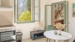 Une cuisine équipée d’un four, d’une poubelle, d’une table à manger avec des chaises et d’une fenêtre avec une porte ouverte.