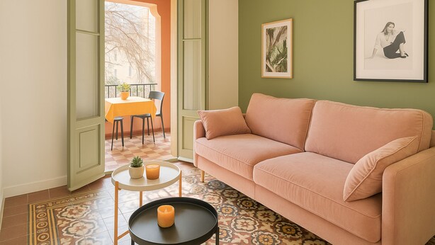 Un salon avec un canapé, une petite table ornée de bougies, un tableau encadré au mur et une vue sur l’extérieur.