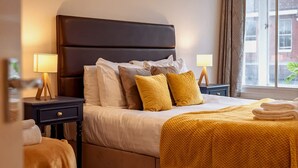 Une chambre d’hôtel avec un lit, deux tables de chevet avec des lampes, une fenêtre avec des rideaux et une vue sur les bâtiments environnants.