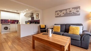 Un salon moderne avec un canapé, une table basse et, au fond, un espace cuisine.