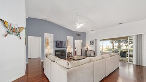A modern living room with a large beige sectional sofa, a fireplace, a ceiling fan, and a view of the outdoors. - Villa S G Spacious 5 Bedroom Family Vacation Home (Inverness)
