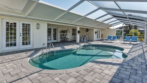 Une piscine extérieure couverte avec un toit en verre, un espace patio avec des chaises et un chemin en briques.