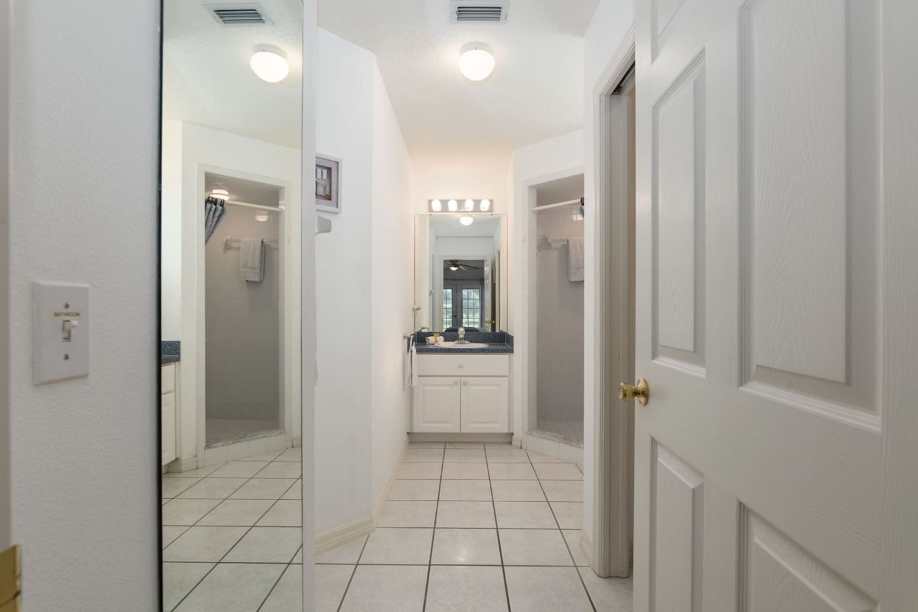 A hallway with a mirror, a vanity with a sink, and a door.