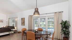 Un coin repas comprenant une table ronde, des chaises, un luminaire suspendu, un canapé, une table basse et une plante en pot.