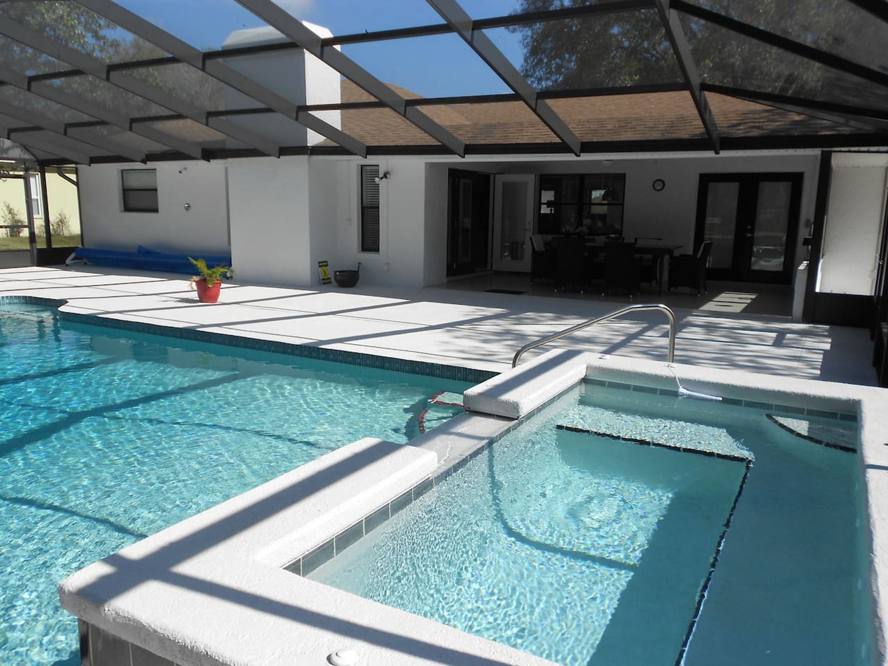 A swimming pool with a sunshade structure, a small plant, and a view of the outside.