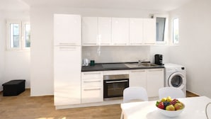 Una cucina moderna con mobili bianchi, un piano di lavoro nero, un lavello, una macchina da caffè e una lavatrice.
