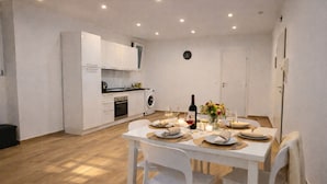 Una cucina compatta con mobili bianchi, un tavolo da pranzo per quattro persone e una sveglia appesa al muro.