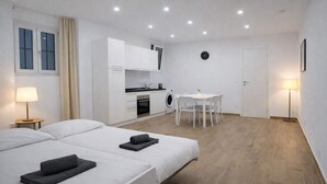 Una camera d'albergo moderna con due letti, angolo cottura, zona pranzo e bagno.