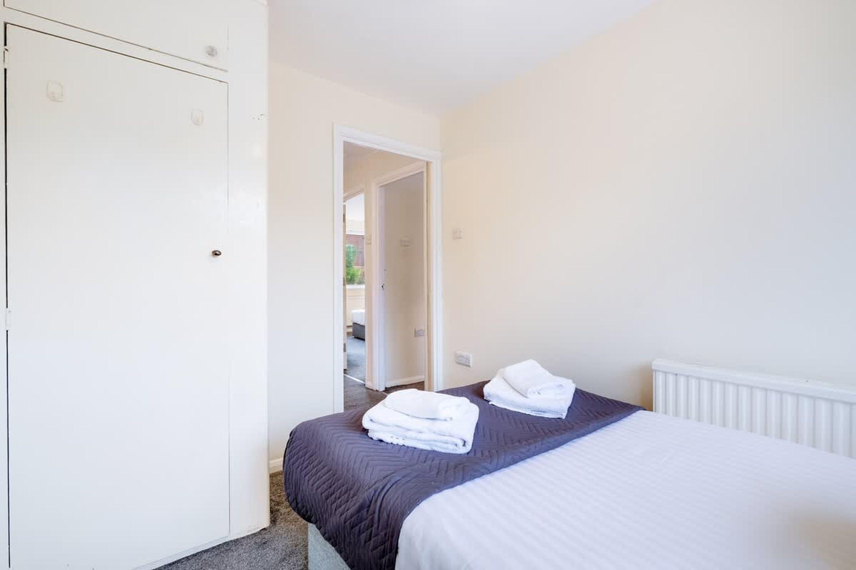 Een slaapkamer met een bed, witte muren, een deur en een radiator.