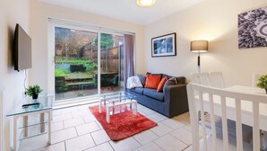 A living room with a sofa, a glass coffee table, a TV, a dining table with chairs, and a sliding glass door leading to a garden. - High Wycombe Home Free Parking Free Wifi Garden (High Wycombe)